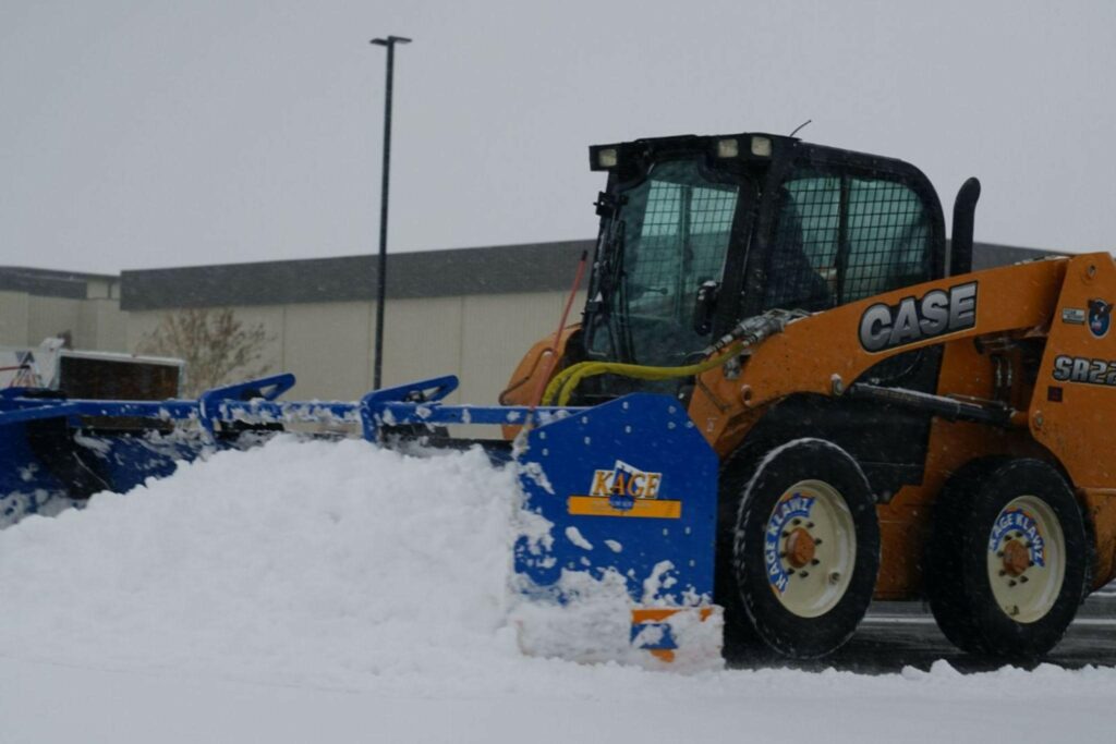 a worker uses a bobcat to clear snow from a parking lot